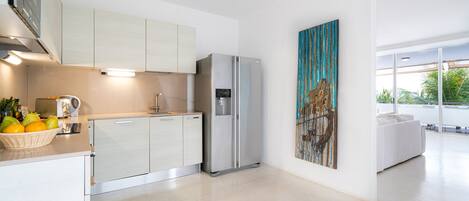 A modern kitchen with white cabinets, a stainless steel refrigerator, and a large window offering a view of the outdoors.