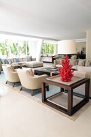 A modern living room with a sofa set, a coffee table with a red coral sculpture, and a large window with a view of greenery.