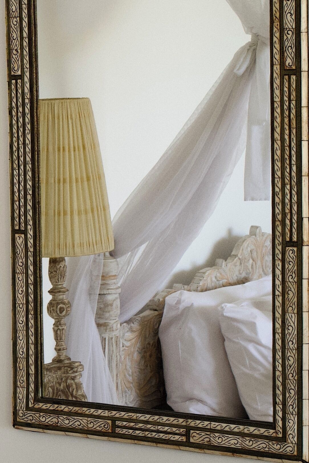 A bed with a canopy, a bedside lamp, and a decorative mirror with an ornate frame.