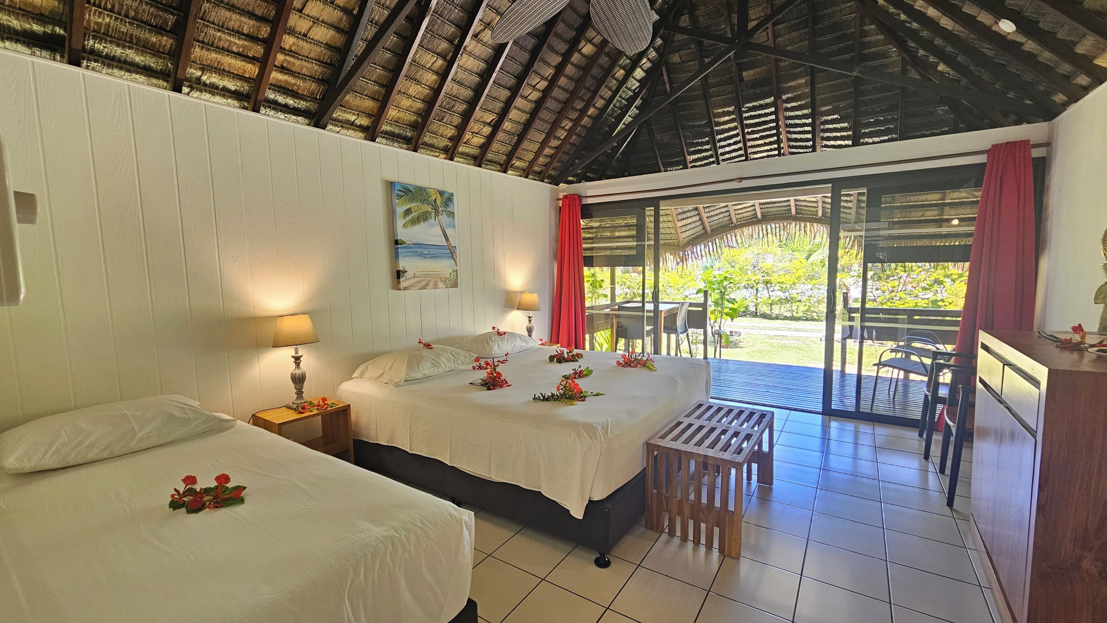 Habitación de hotel con dos camas, una mesita, una banca y vistas al exterior.