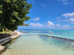 A beach with clear turquoise water, a sandy shore, and a stone pathway leading to the water. - Hotel Hibiscus (Moorea-Maiao)