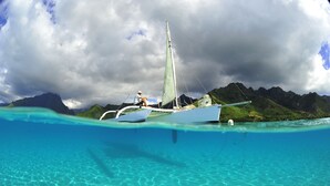 Un bateau sur une eau turquoise et limpide, avec une personne à bord, entouré de collines verdoyantes et sous un ciel nuageux.