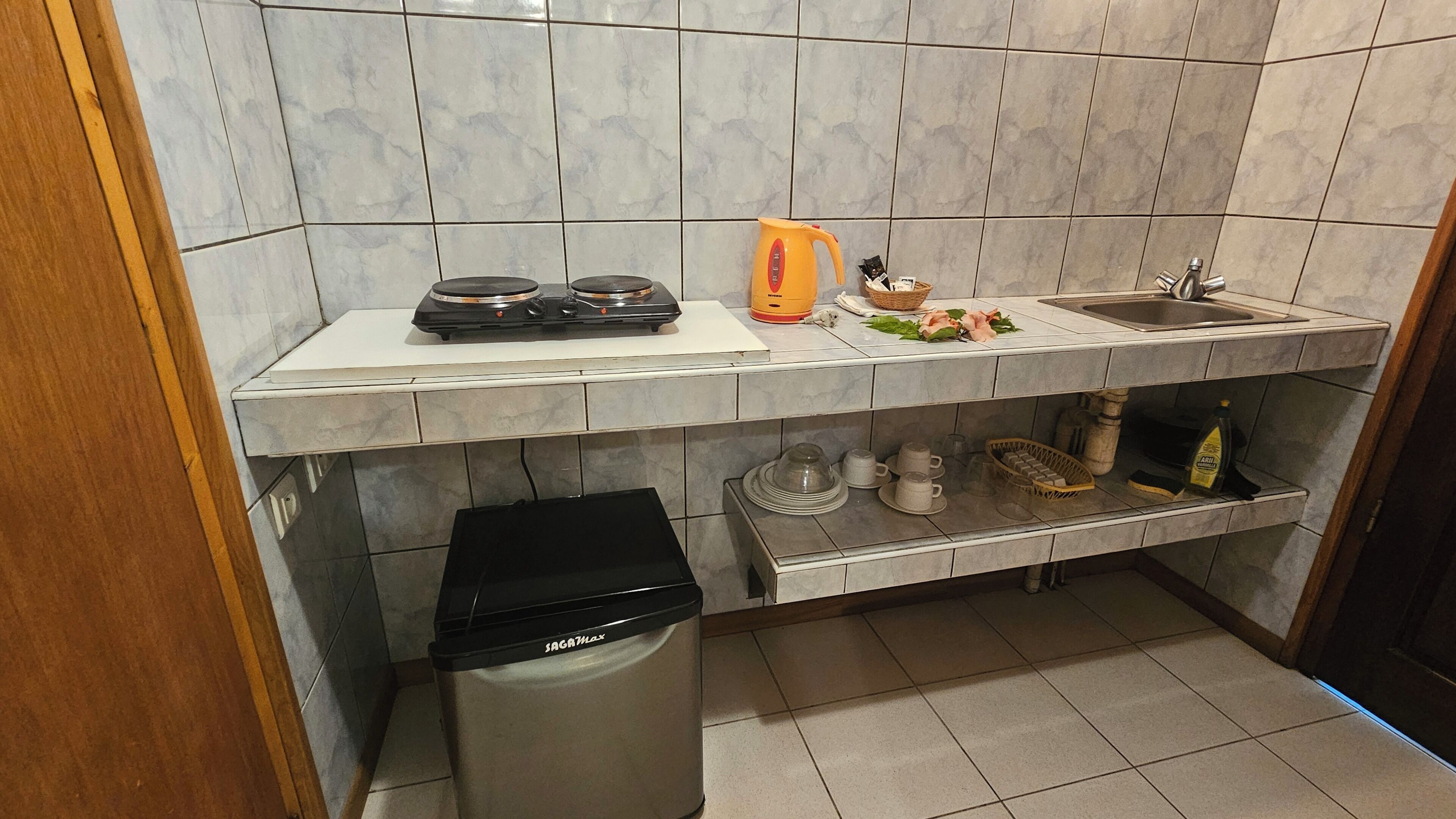 Una cuina amb fogó de gas, un rentaplat i un gresol, i una estantalia amb utensilis de cuina.