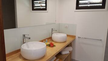Un baño moderno con dos lavamanos blancos, un mueble de tocador de madera, un perchero para toallas y un espejo.