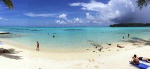 A beach with clear turquoise water, people sunbathing, and a boat in the water. - Hotel Hibiscus (Moorea-Maiao)