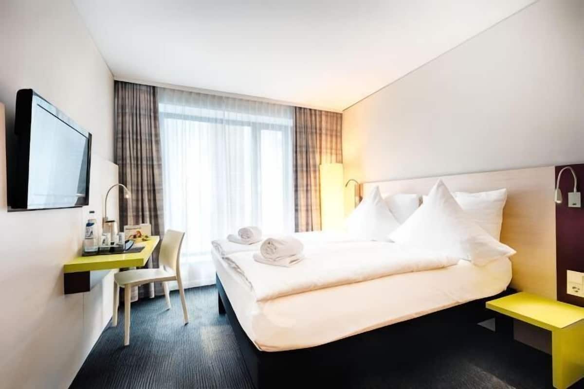 Une chambre d’hôtel équipée d’un lit, d’un bureau, d’une chaise et d’un téléviseur fixé au mur.
