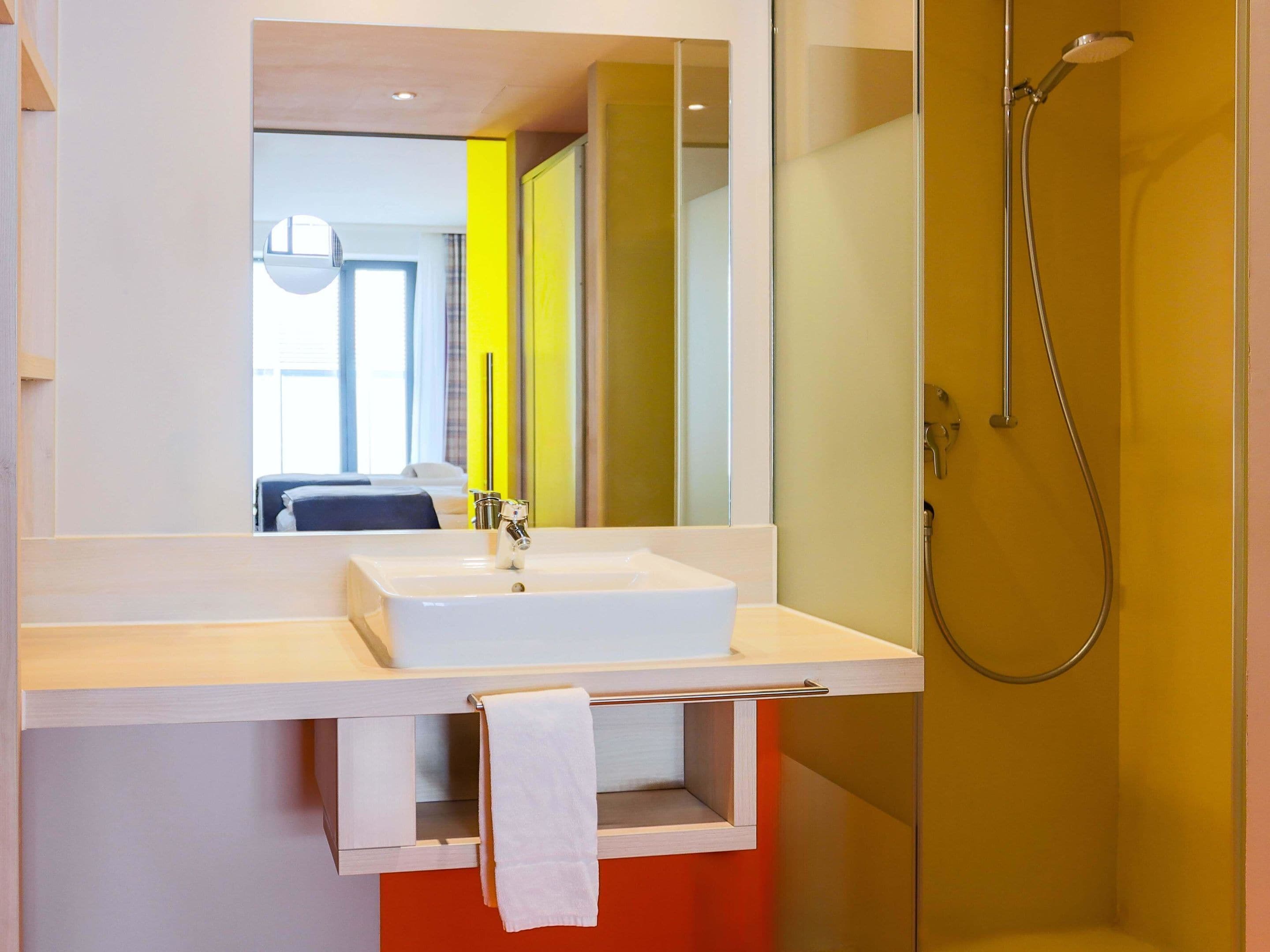 Un bagno moderno con un lavandino bianco, uno specchio e una doccia.