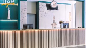 Una recepción con un cartel que dice 'BAR everyone', el logotipo de B&B Hotels y una pared decorativa con un mural de aves.