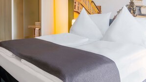 Una habitación de hotel con una cama, almohadas, una mesita de noche y un mural en la pared de un edificio.