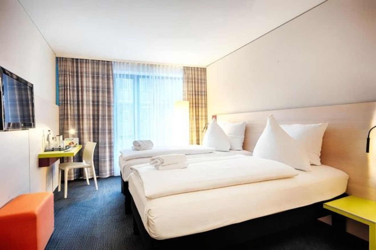 Una habitación de hotel con cama, escritorio, silla y televisor montado en la pared.