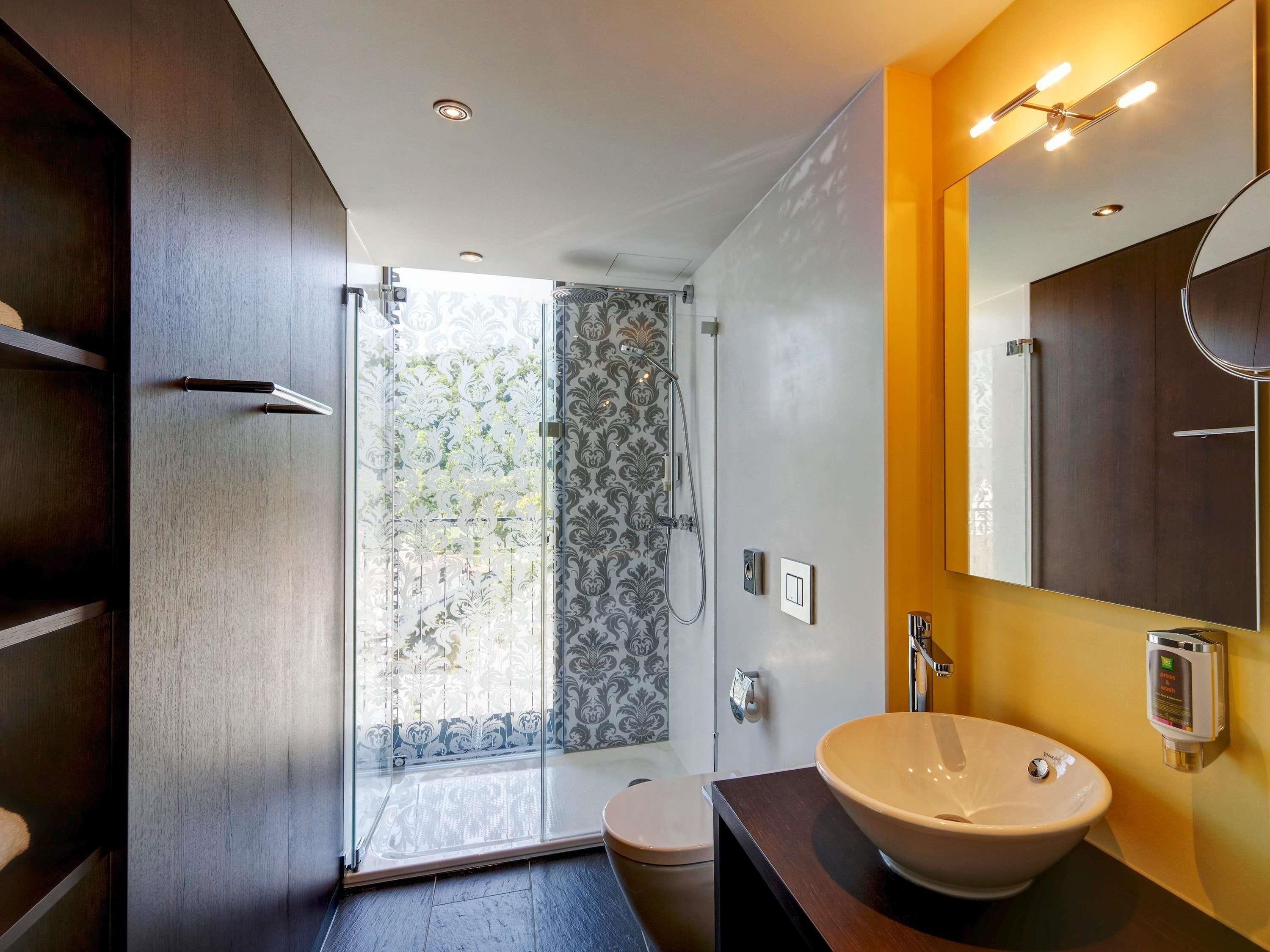Un baño moderno con mampara de vidrio, inodoro y un lavamanos grande.