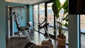 Un gimnasio con equipo de ejercicio, ventanas amplias y vistas a la ciudad.