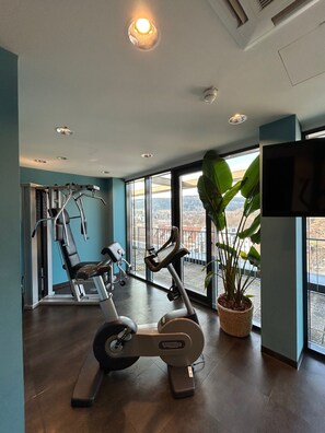 Un gimnasio con equipo de ejercicio, ventanas amplias y vistas a la ciudad.