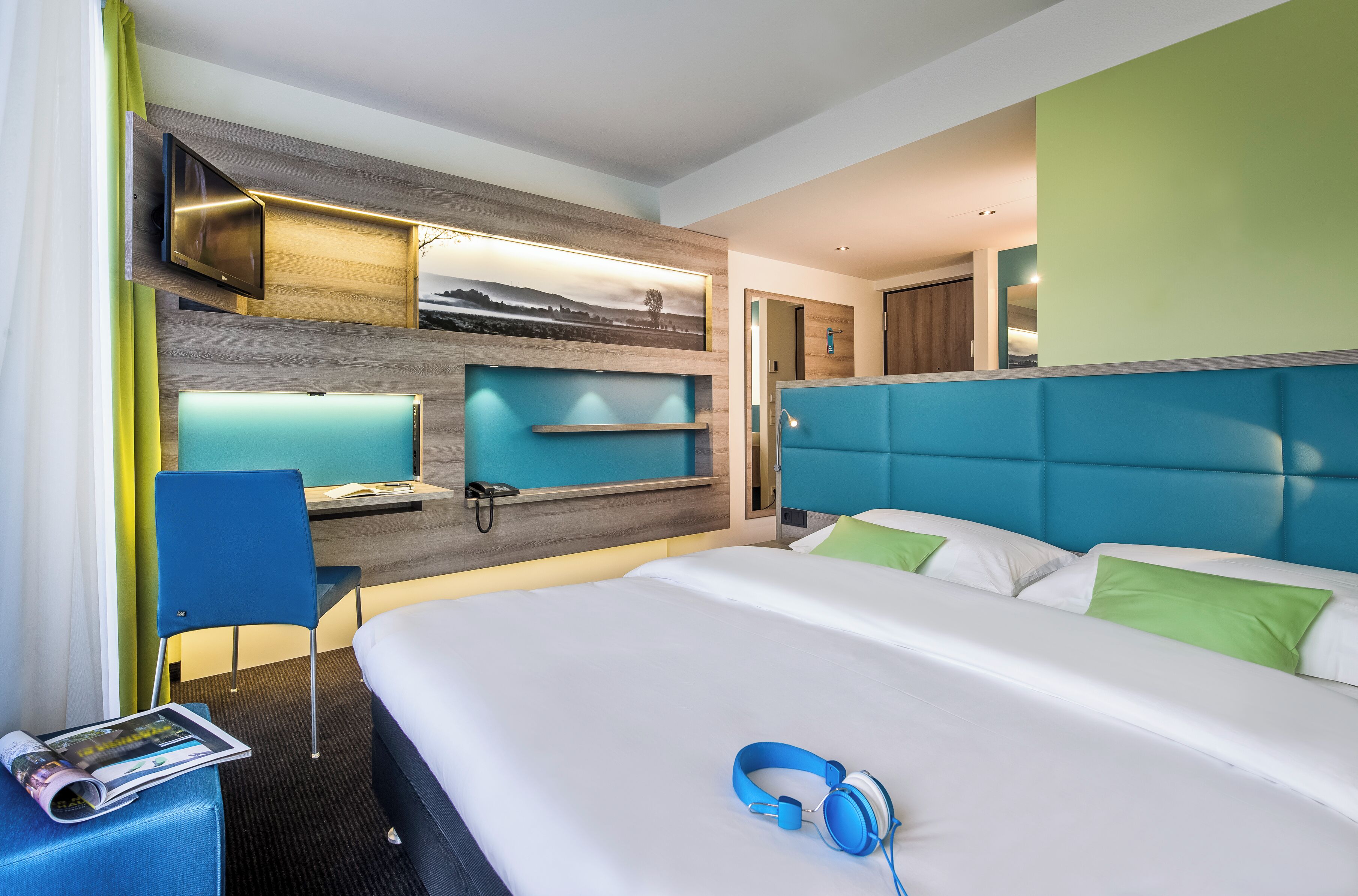 Une chambre d’hôtel moderne dotée d’un grand lit, d’un bureau avec un ordinateur, d’un téléviseur fixé au mur et offrant une vue sur l’extérieur.
