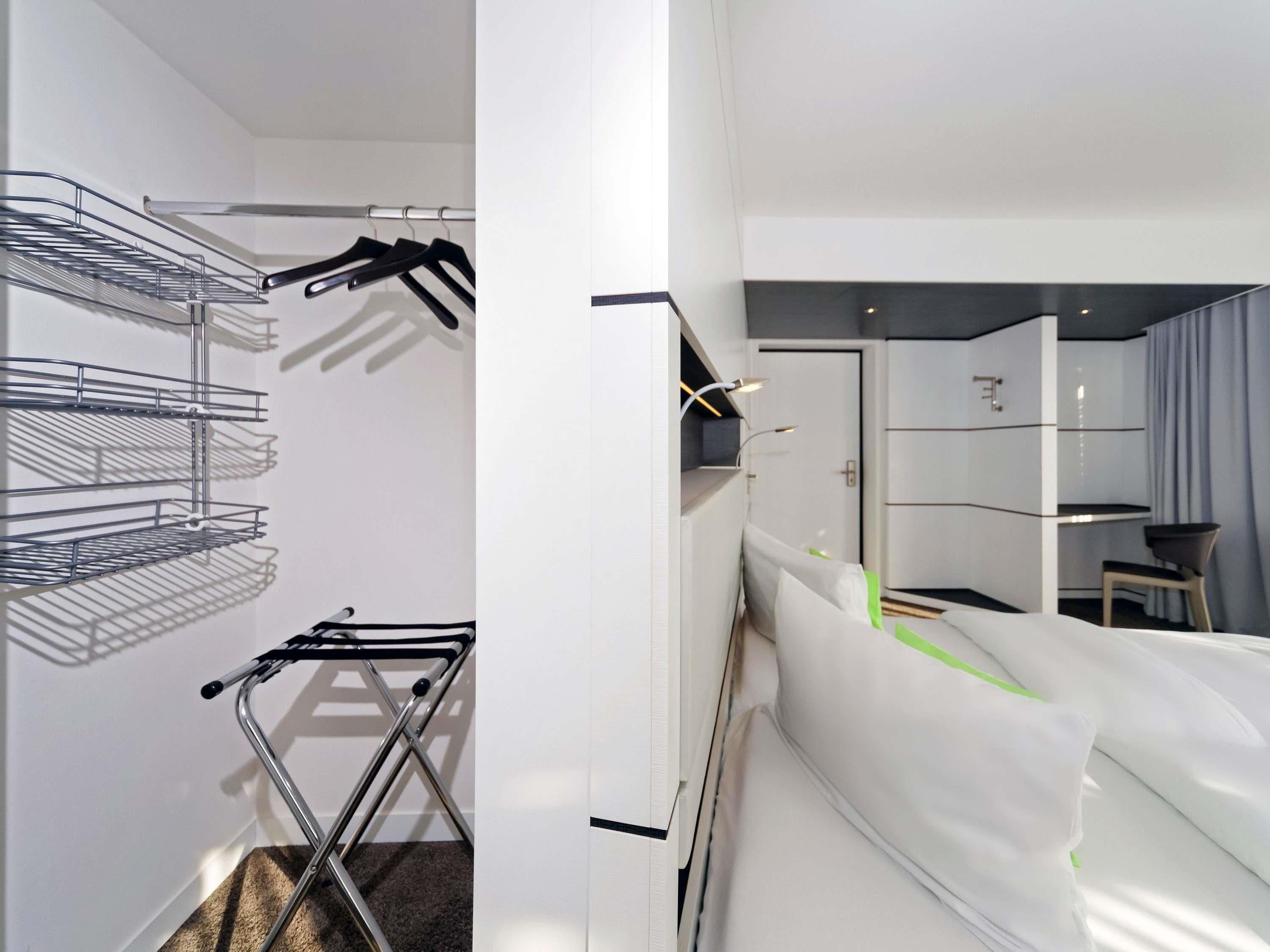 A hotel room with a metal drying rack, a bed with white bedding, a small table, and a chair.