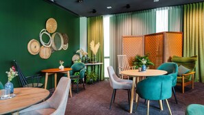 Una habitación con pared verde, una mesa redonda de madera y sillas color turquesa.