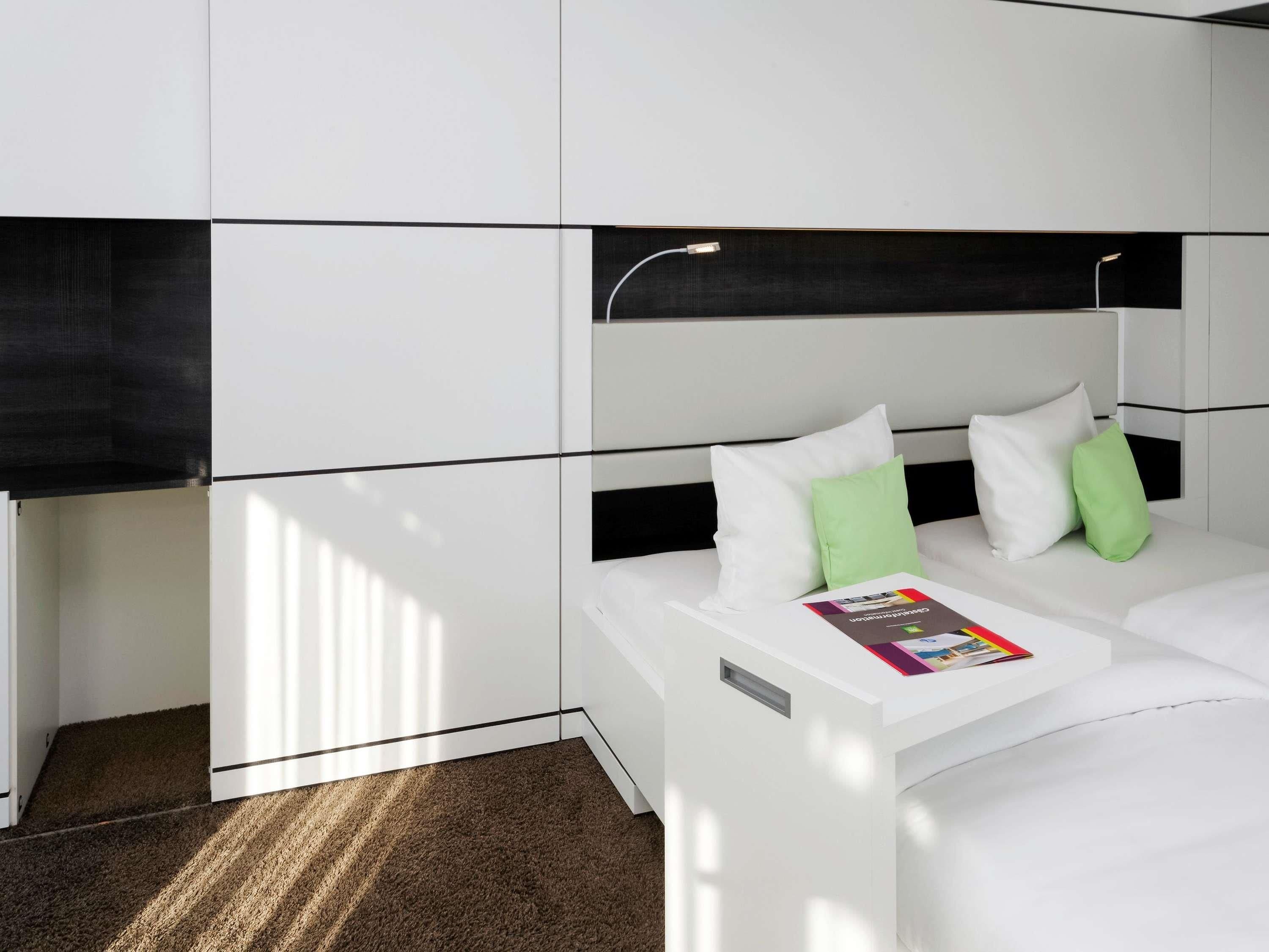 A modern hotel room with a white bed, two pillows, a magazine on the bed, and a black headboard.