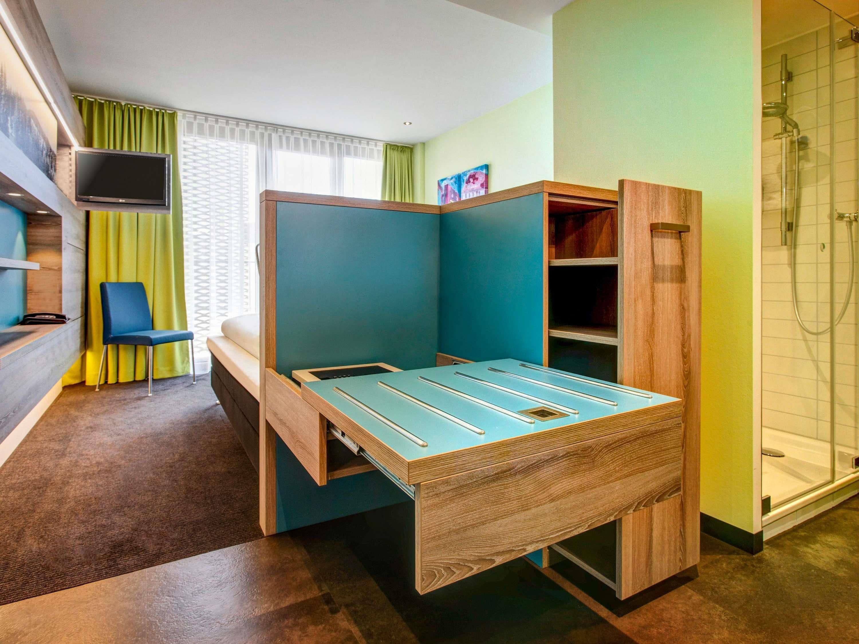 A compact room with a foldable bed, a TV, a chair, and a shower.