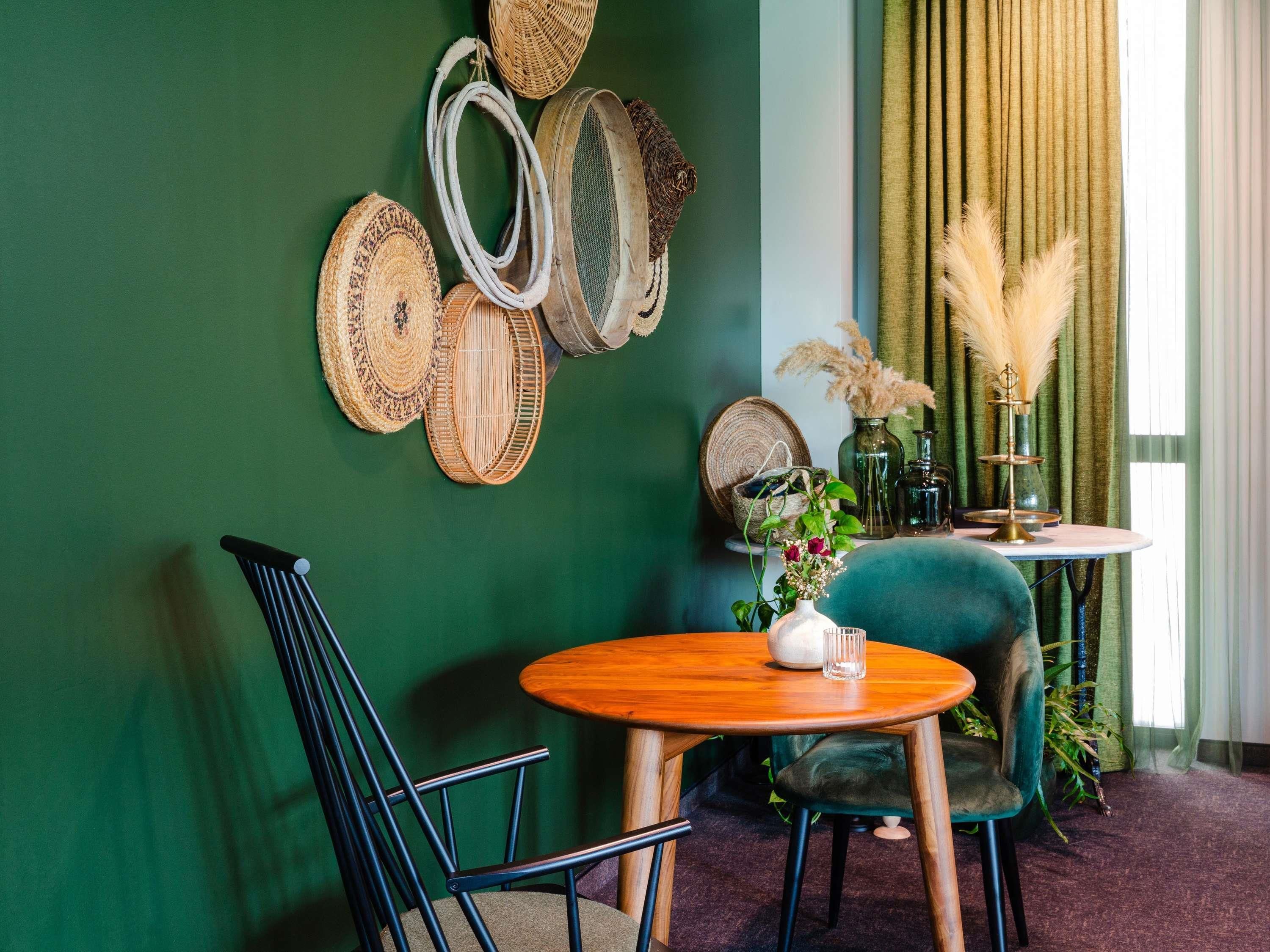 Una habitación con una pared verde, una mesa redonda de madera, una silla verde azulada y una silla negra.