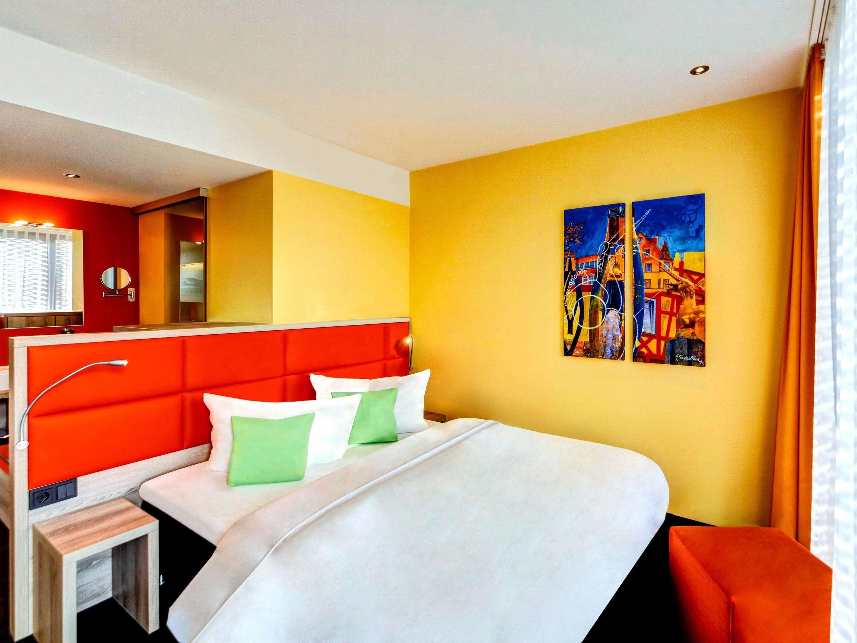 Een hotelkamer met een bed, nachtkastje, spiegel en een schilderij aan de muur.