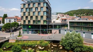Un hotel moderno con fachada de vidrio, varios pisos y una terraza en la azotea.