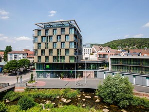Un hotel moderno con fachada de vidrio, varios pisos y una terraza en la azotea.
