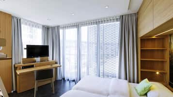 Ein modernes Hotelzimmer mit Bett, Schreibtisch und Fernseher sowie großen Fenstern mit Vorhängen.