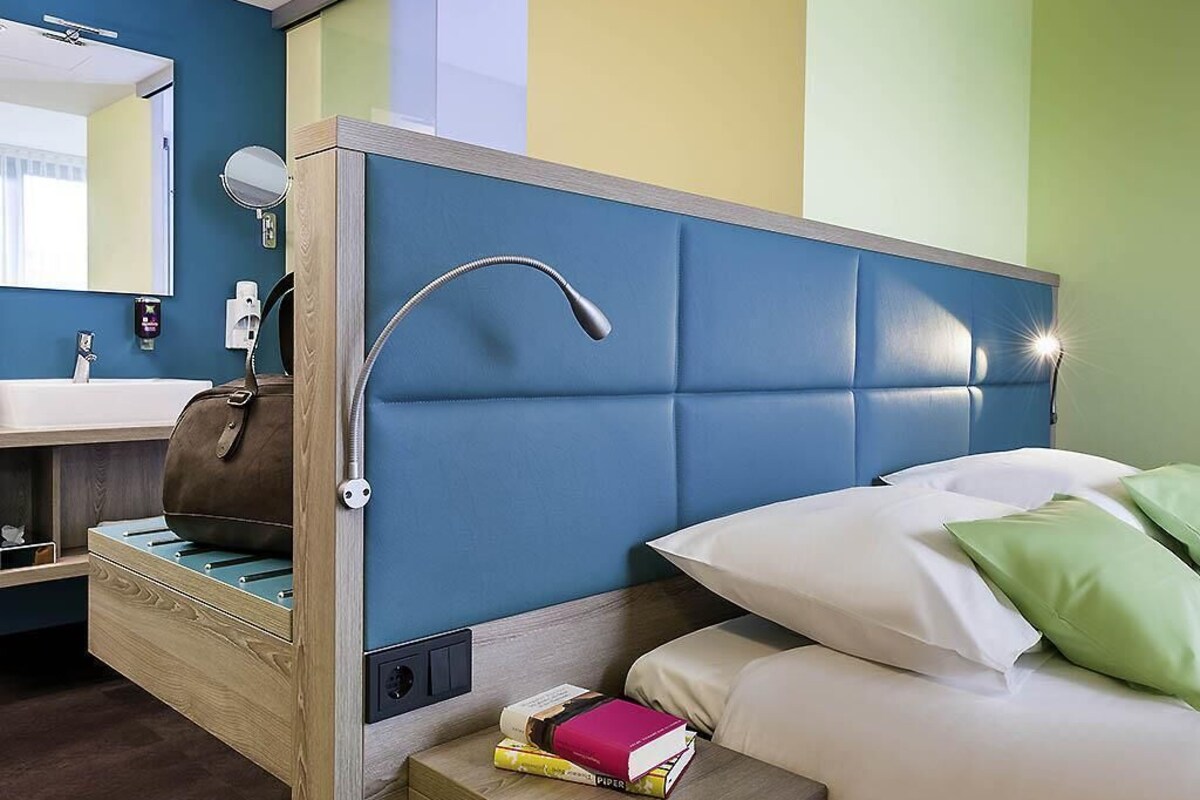 Una habitación de hotel con cama, mesita de noche y baño con espejo y lavamanos.