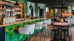 Zona de bar con pared de azulejos verdes, estantes con botellas y taburetes.