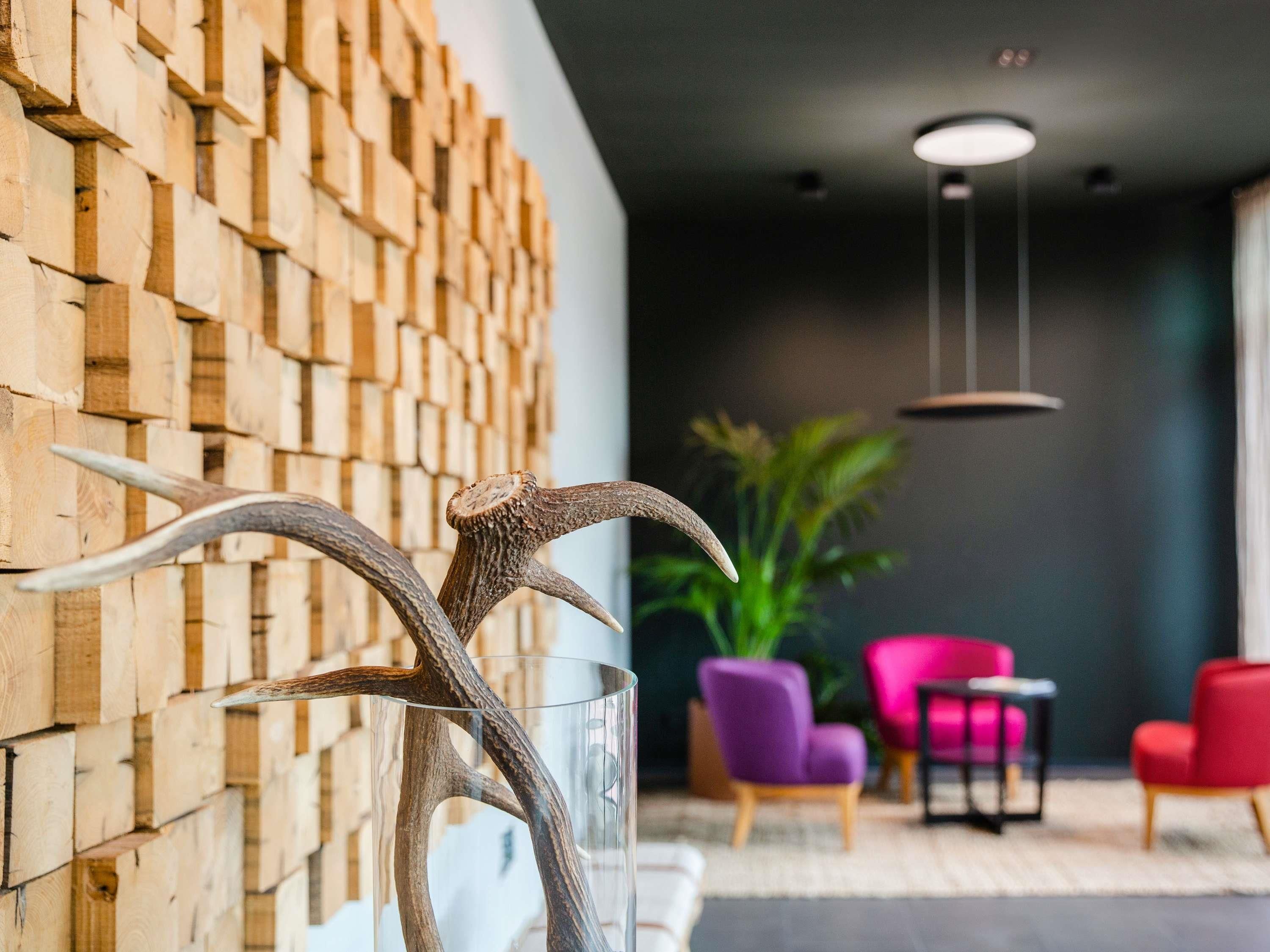 A modern interior with a wooden wall, a glass vase with antlers, and a seating area with chairs and a plant.
