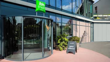A modern hotel entrance with a glass facade, a green 'ibis Styles' sign, and a welcome sign.