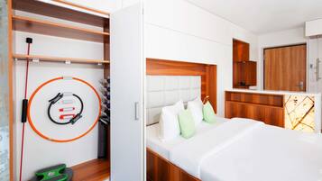A hotel room with a bed, a wardrobe, a small seating area, and a wall-mounted exercise equipment.