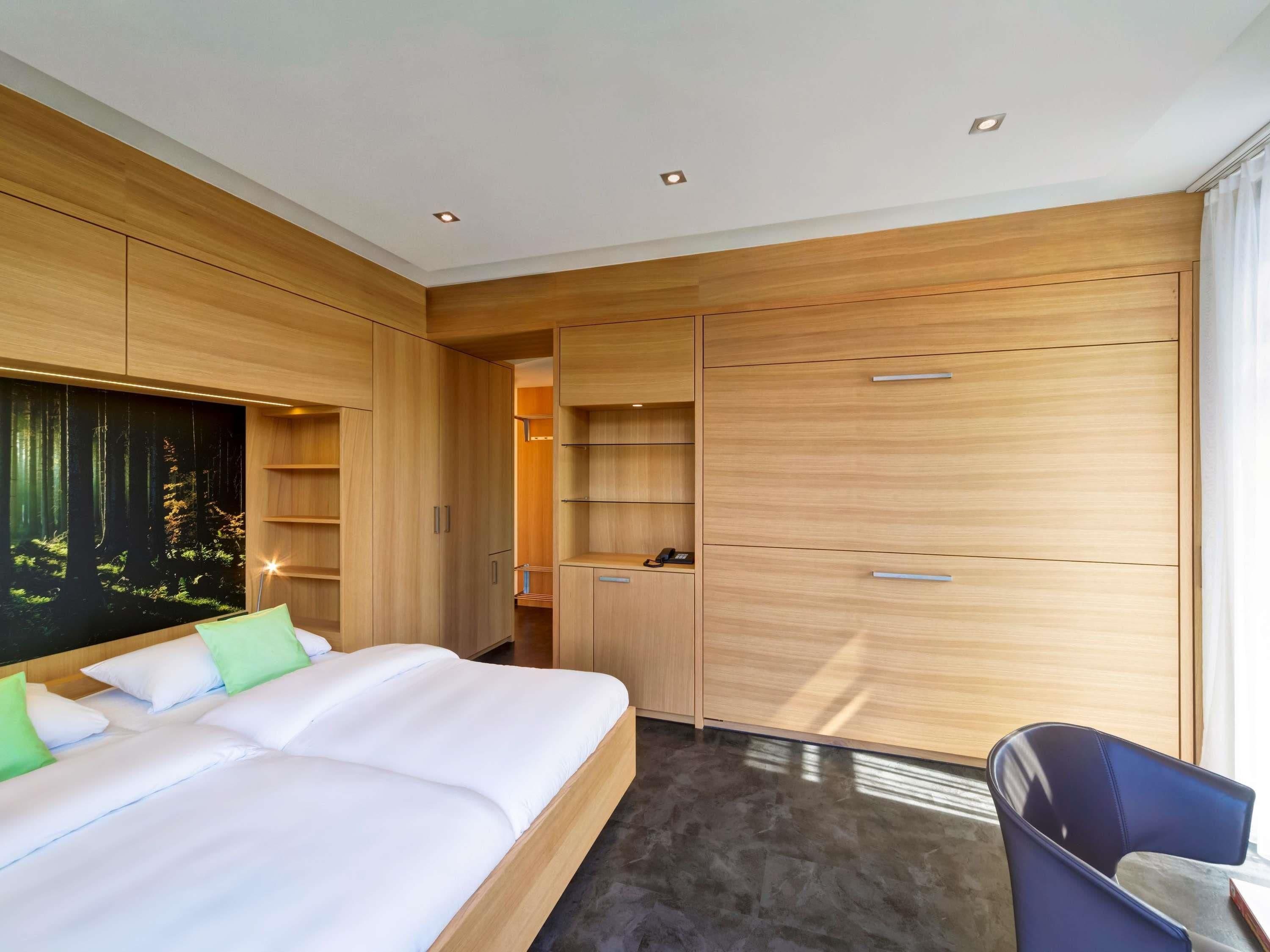 Una habitación de hotel moderna con una cama grande, un armario de madera y estanterías empotradas.