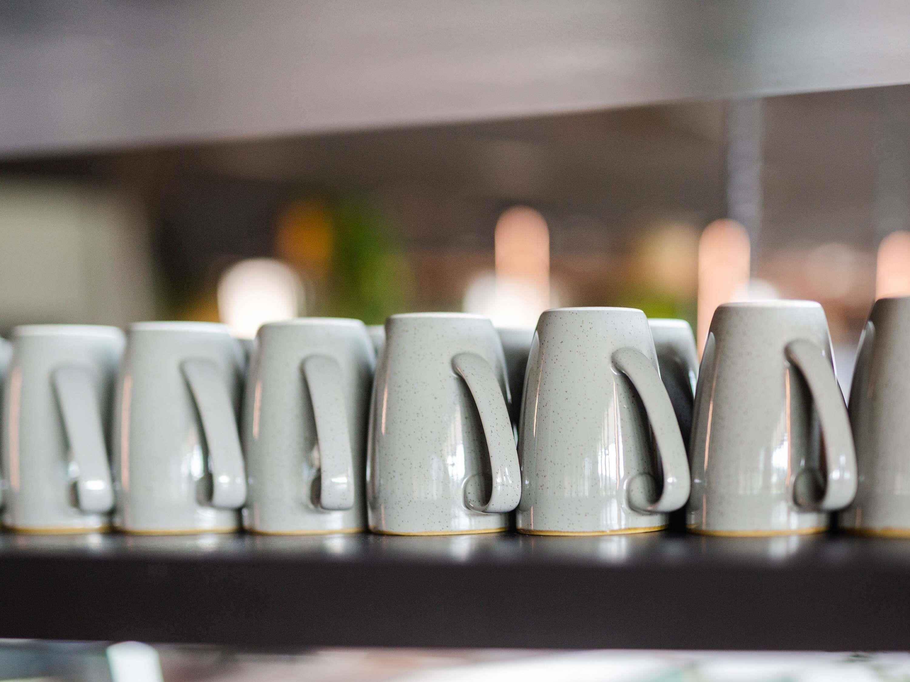 Una fila de tasses ceràmiques grises amb anses sobre una prestatgeria.