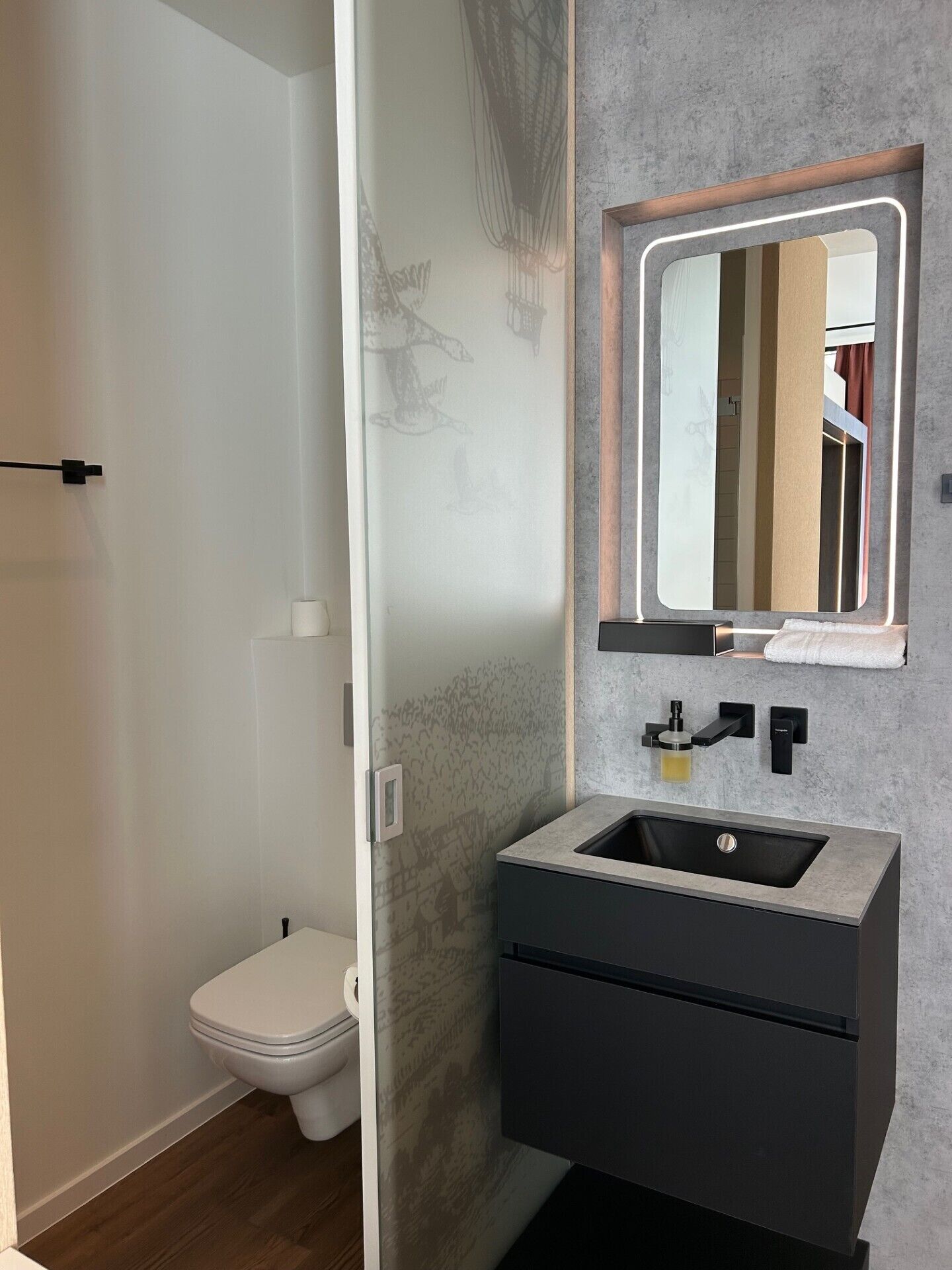 A modern bathroom with a built-in sink, a mirror with integrated lighting, and a toilet.