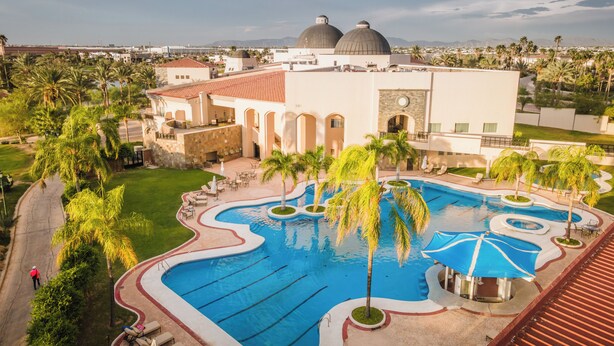 A resort with a large swimming pool, palm trees, and a building with domed roofs. - Azul Talavera Country Club (Torreón)