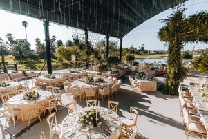 Un lugar para bodas al aire libre con mesas redondas, sillas y centros de mesa florales.