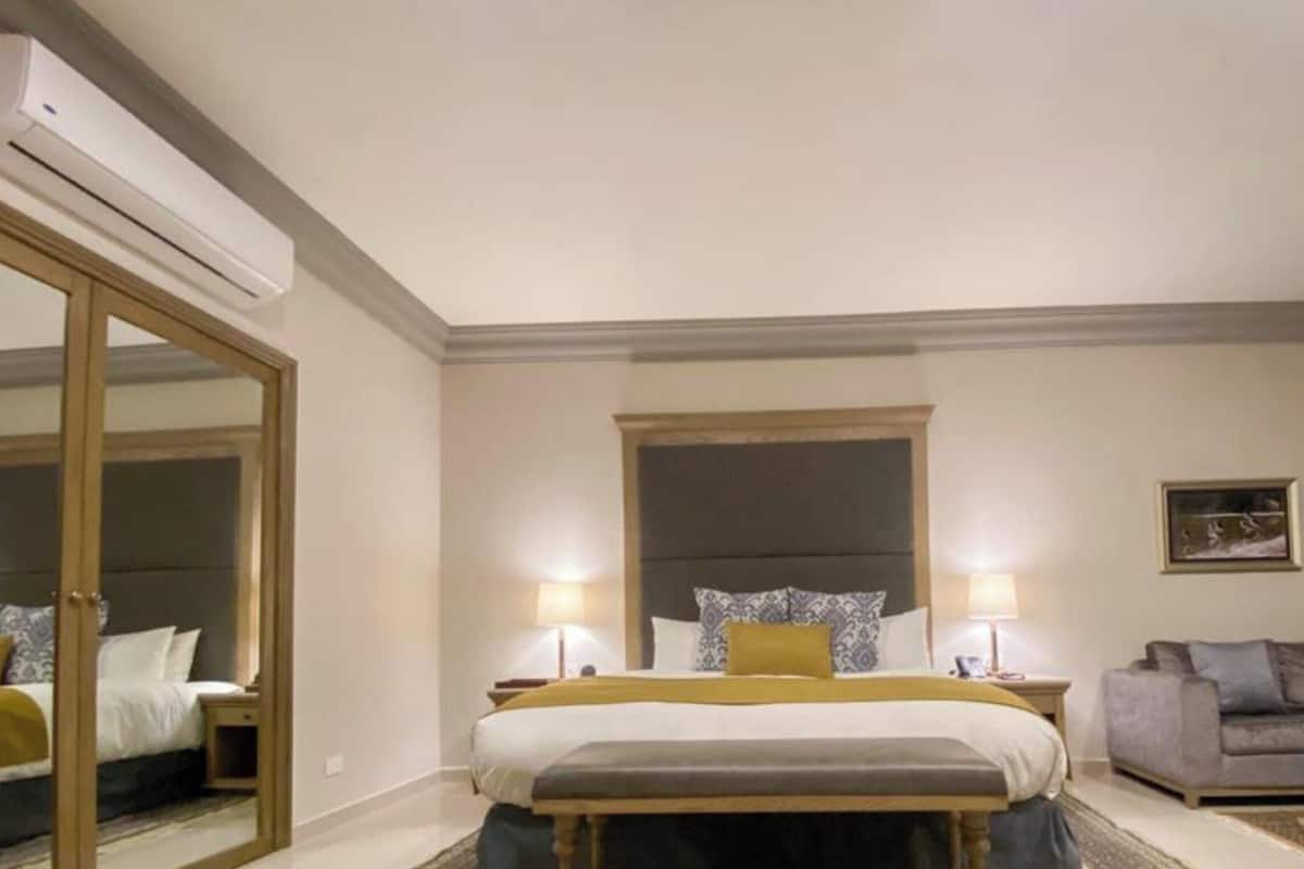 Habitación de hotel con cama, mesitas de noche, un sofá, un espejo y un cuadro en la pared.