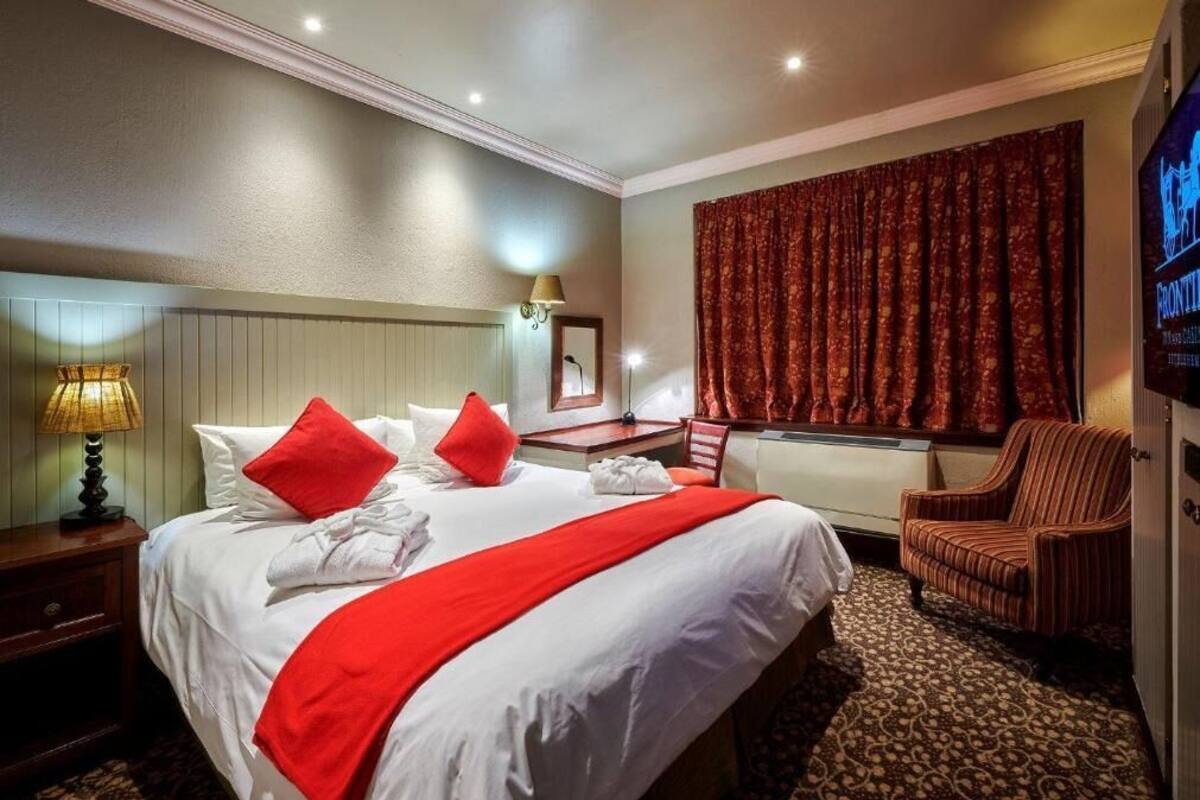A hotel room with a large bed, a chair, a desk, a lamp, and a television.