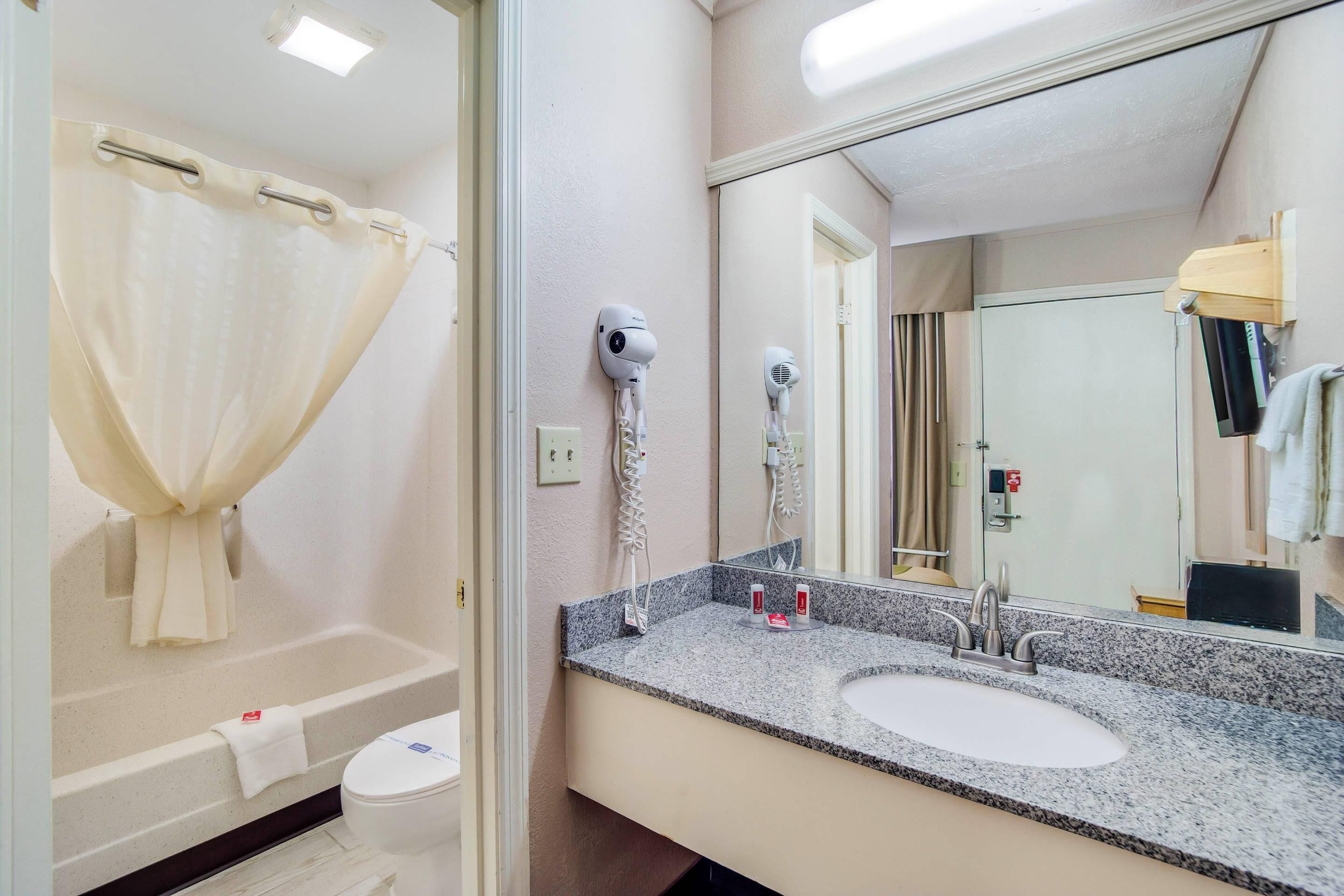 A bathroom with a bathtub, a sink, a mirror, and two hair dryers mounted on the wall.