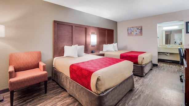 Habitación de hotel con dos camas, una silla, un escritorio y un espejo.
