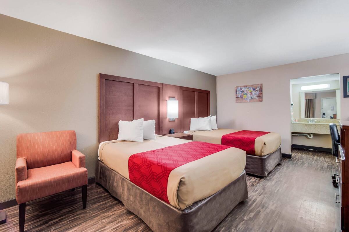 Habitación de hotel con dos camas, una silla, un escritorio y un espejo.