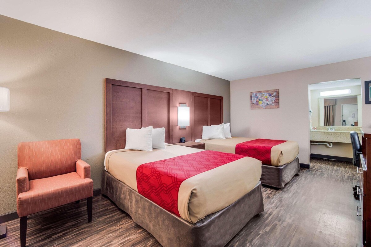 Une chambre d’hôtel avec deux lits, une chaise, un bureau et un miroir dans la salle de bain.