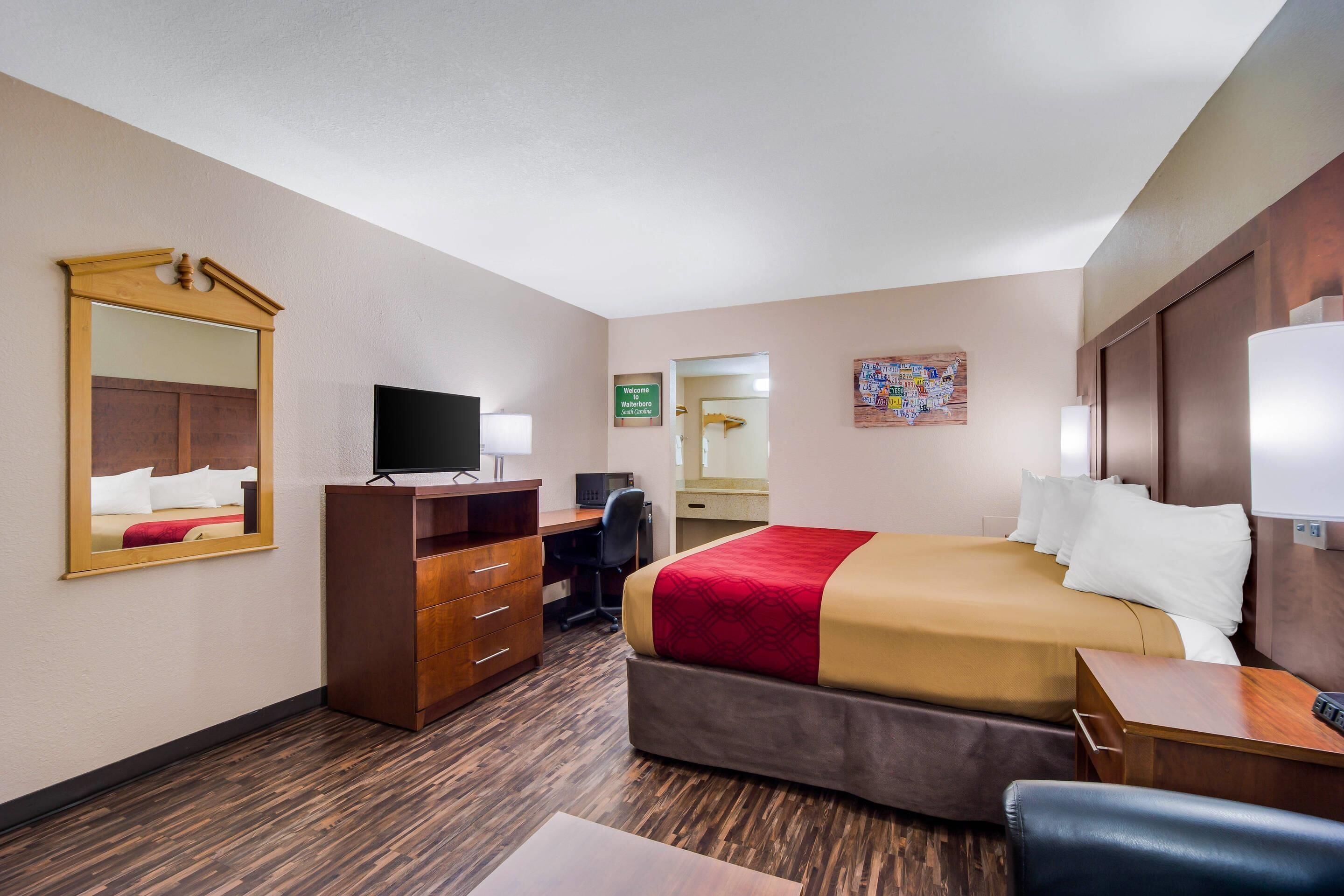 Ein Hotelzimmer mit Bett, Schreibtisch, Stuhl, Fernseher und Spiegel.