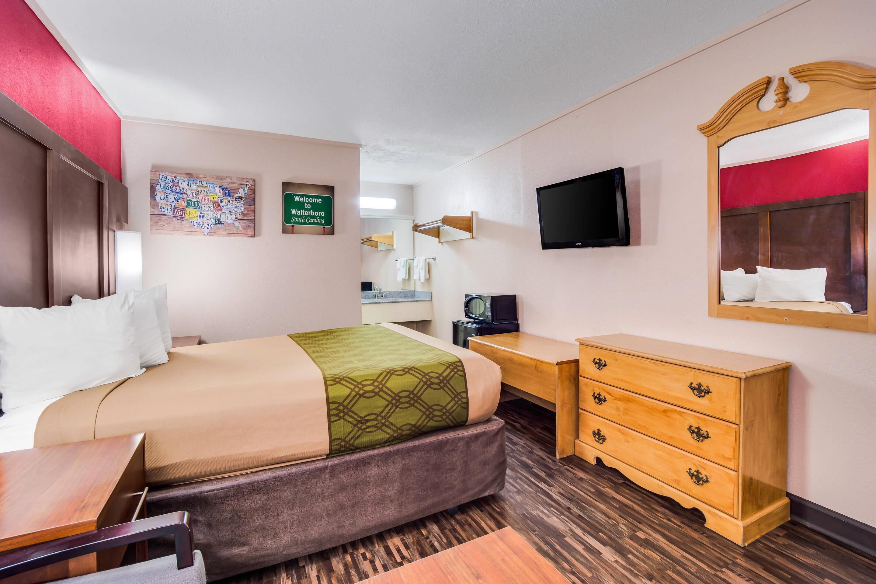 Une chambre d’hôtel équipée d’un lit, d’un bureau, d’une commode, d’une télévision et d’un miroir fixé au mur.