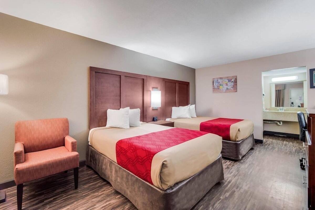 Una habitación de hotel con dos camas, una silla, un escritorio y un espejo.