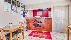 Zona de recepción con un escritorio de madera, premios enmarcados y una alfombra roja con el nombre del hotel.
