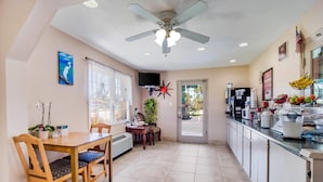 Una cocina con una mesa de comedor, sillas, un ventilador de techo, un televisor y una puerta que da al exterior.