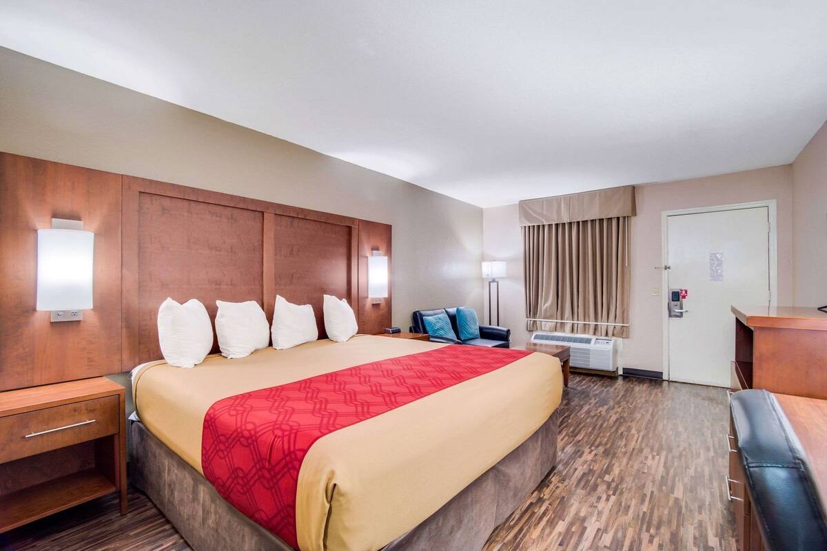 Habitación de hotel con una cama grande, mesitas de noche, un escritorio, una silla, un armario, un espejo y una ventana con cortinas.