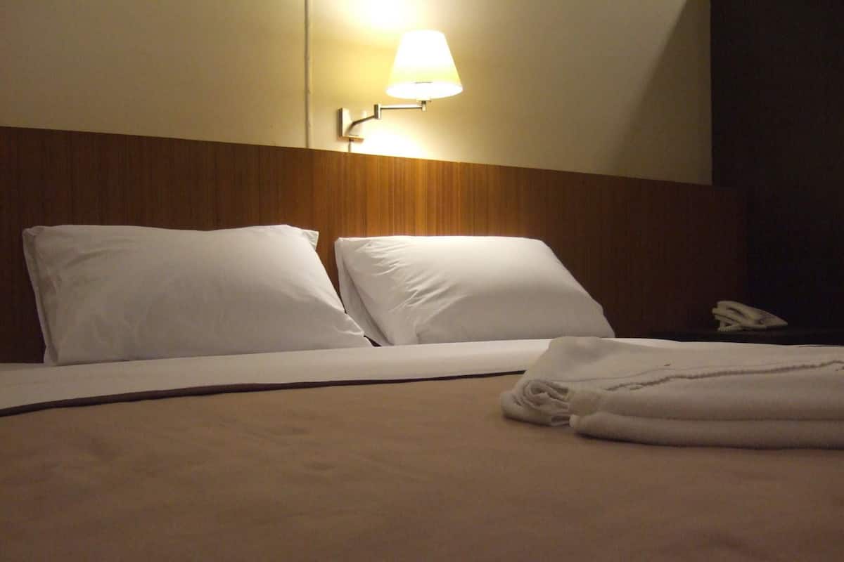 A neatly made bed with white linens, a wall-mounted lamp, and a telephone on a bedside table.